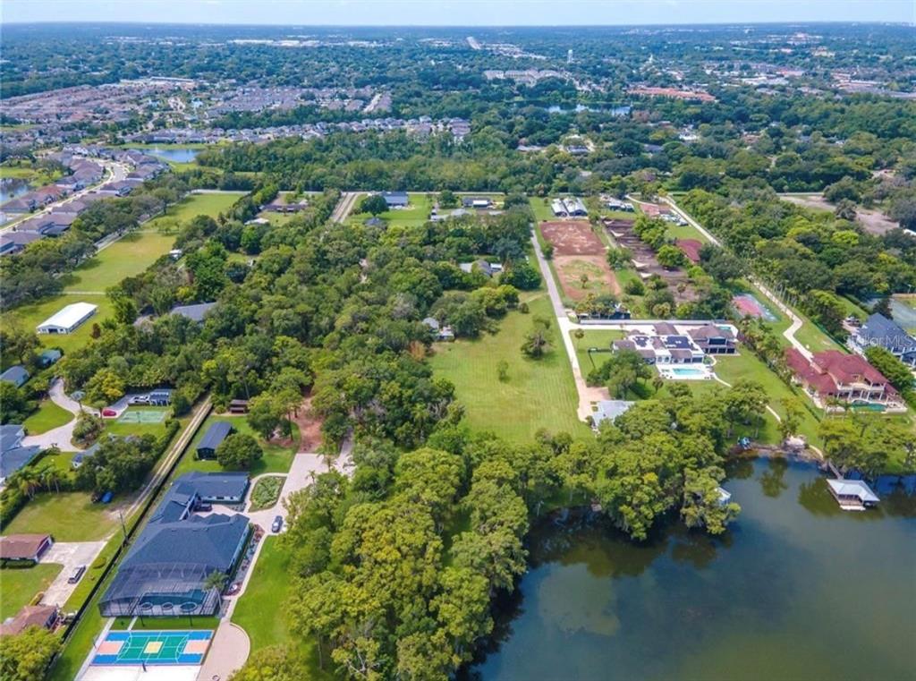 An aerial view shows several large houses with swimming pools and tennis courts near a lake — 1133 BELLA LAGO COVE, WINTER PARK, FL