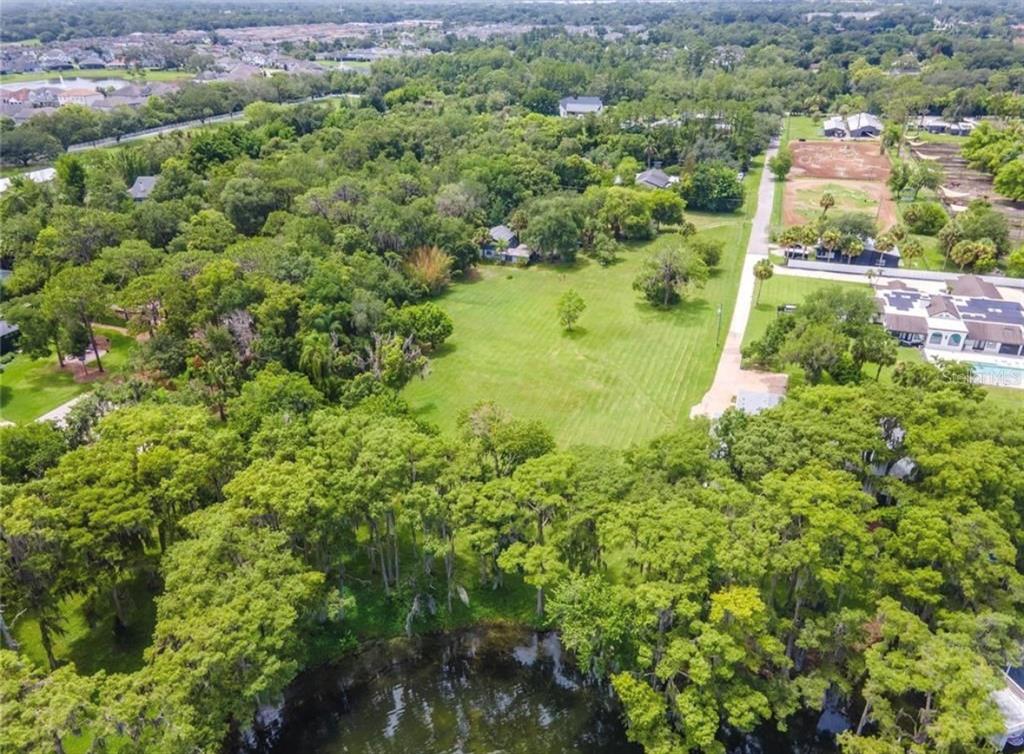 An aerial view shows a large grassy lot surrounded by trees and a small pond — 1133 BELLA LAGO COVE, WINTER PARK, FL