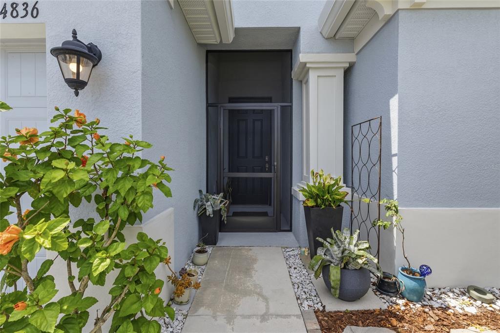 A front entryway features a screen door, potted plants, and a light fixture on the wall — 4836 REISSWOOD LOOP, PALMETTO, FL