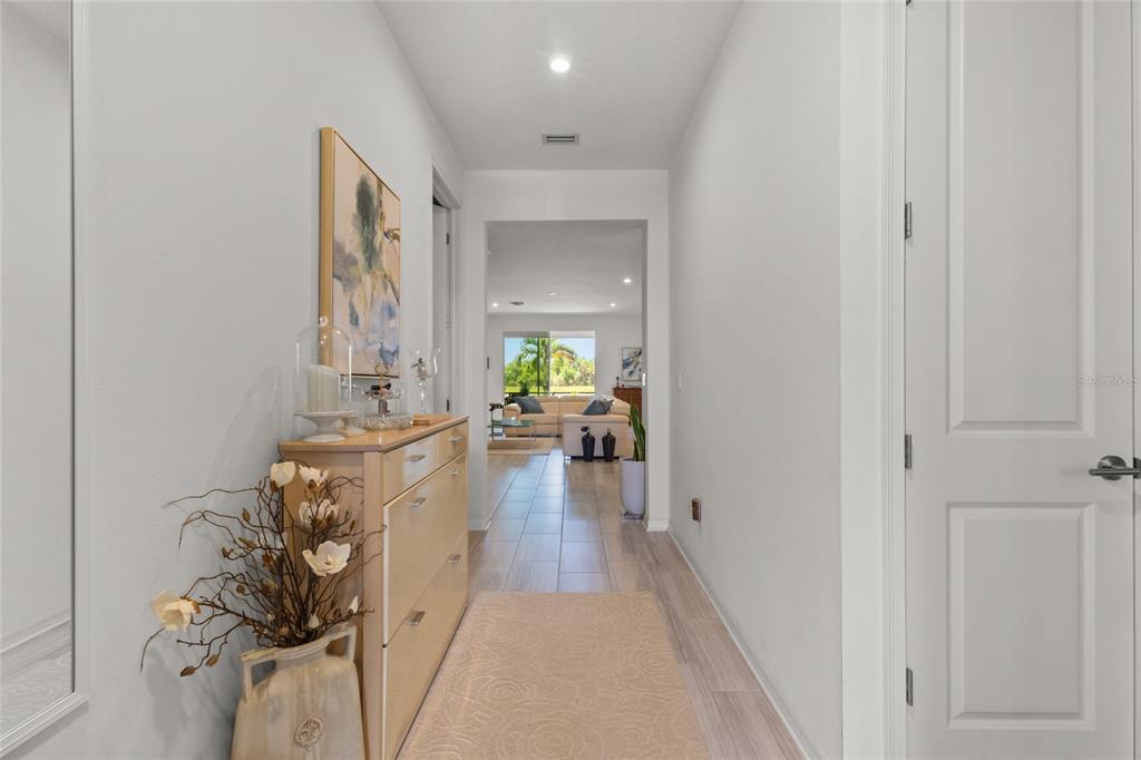 A hallway with light wood-look flooring leads to a living area with a view outside — 4836 REISSWOOD LOOP, PALMETTO, FL