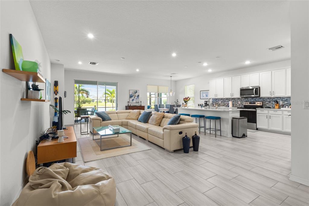 An open-concept living room and kitchen featuring light tile floors and a large sectional sofa — 4836 REISSWOOD LOOP, PALMETTO, FL