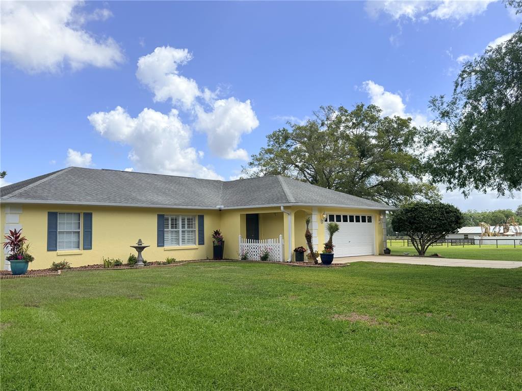 A yellow single-story house with blue shutters and a white garage door sits on grass — 331 SE HIGHWAY 42, SUMMERFIELD, FL