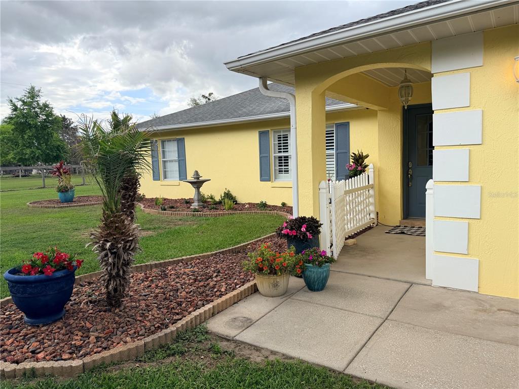 A yellow house exterior features a covered porch, blue shutters, and a landscaped front yard — 331 SE HIGHWAY 42, SUMMERFIELD, FL