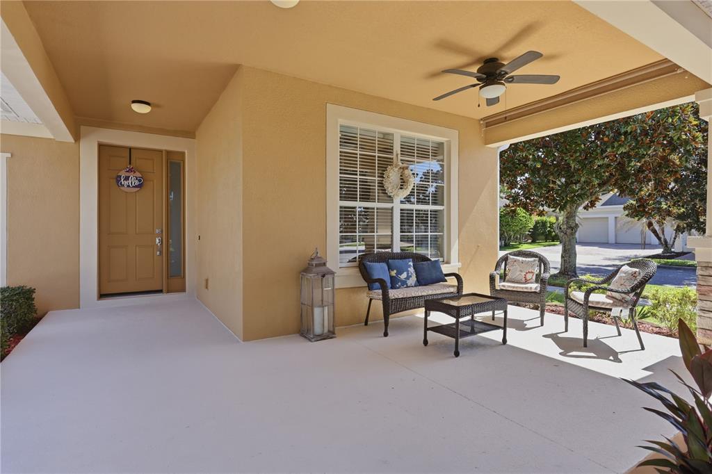 A covered front porch features tan walls, a ceiling fan, and wicker patio furniture — 13231 ROXBORO ROAD, WINDERMERE, FL