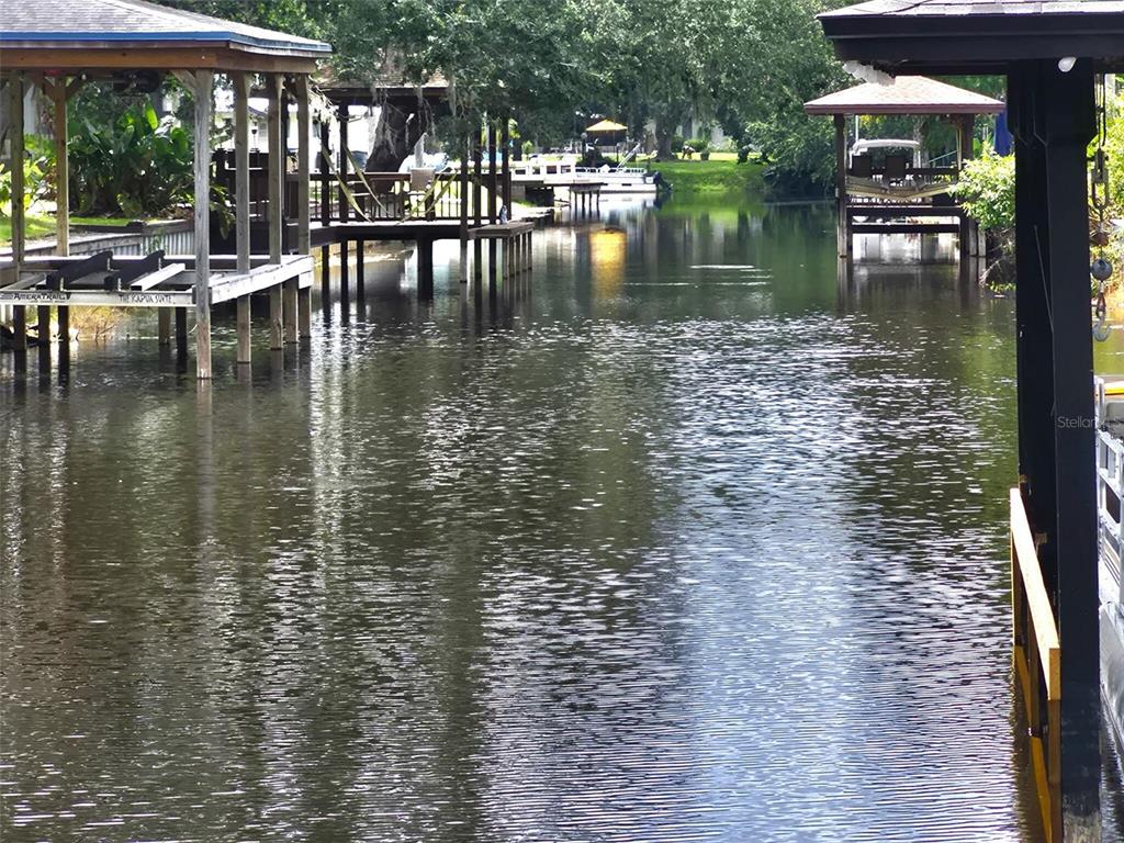 A canal view featuring multiple wooden boat docks and covered slips under lush green trees — 5370 WHISPERING PINE CIRCLE, ST CLOUD, FL