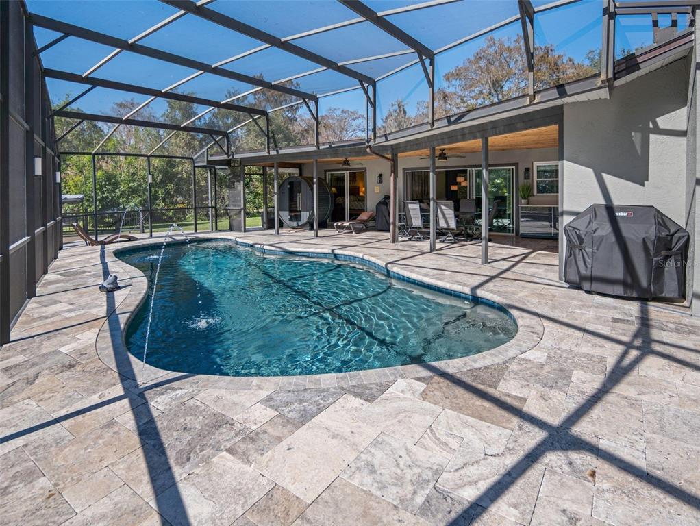 A screened-in patio features a kidney-shaped swimming pool with stone pavers and a covered area — 5370 WHISPERING PINE CIRCLE, ST CLOUD, FL