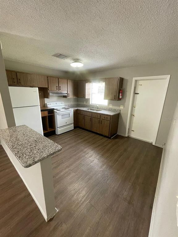 A kitchen features wood cabinets, granite-look countertops, white appliances, and wood-look flooring — 160 N NEKOMA AVENUE UNIT 1, LAKE ALFRED, FL