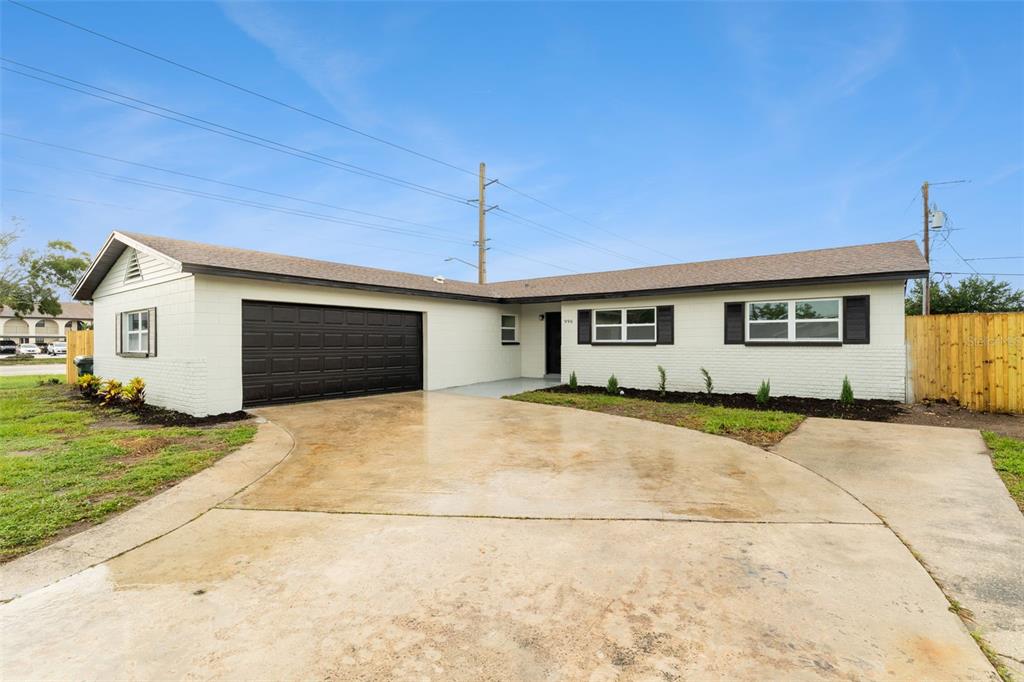 A single-story house with a white brick exterior, a dark garage door, and a concrete driveway — 996 SARAZEN DRIVE, ROCKLEDGE, FL