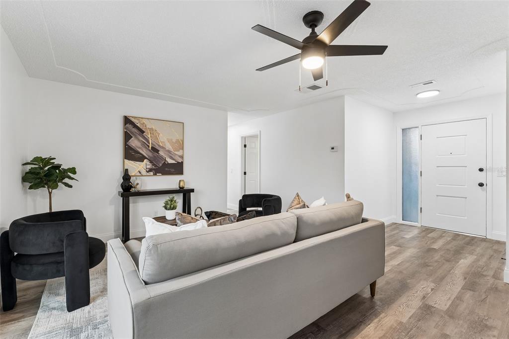A living room features a grey sofa, black chairs, a ceiling fan, and wood-look flooring — 996 SARAZEN DRIVE, ROCKLEDGE, FL