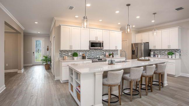 A modern kitchen features white cabinets, a large quartz island with stools, and wood-look flooring — 15 CYLAMEN COURT, HOMOSASSA, FL