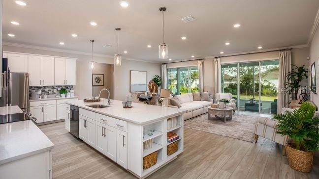 An open-concept kitchen with a large white island overlooks a living room with sliding doors — 15 CYLAMEN COURT, HOMOSASSA, FL
