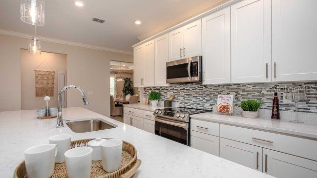 A modern kitchen features white cabinets, a quartz island with a sink, and stainless appliances — 15 CYLAMEN COURT, HOMOSASSA, FL