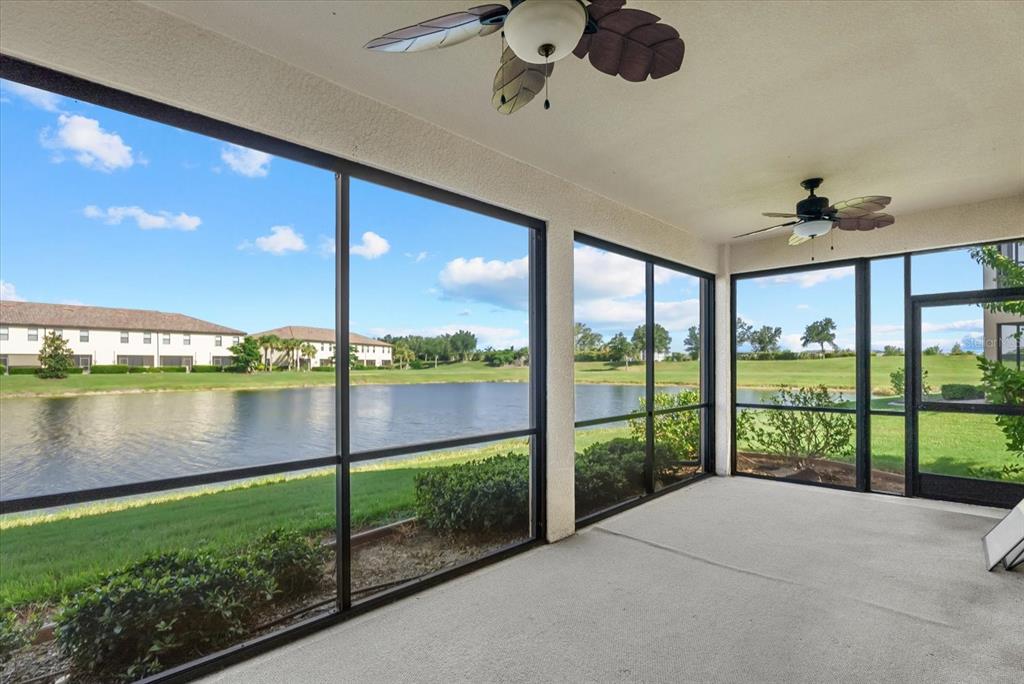 A screened-in patio with two ceiling fans overlooks a lake and grassy landscape — 20150 RAGAZZA CIRCLE UNIT 102, VENICE, FL