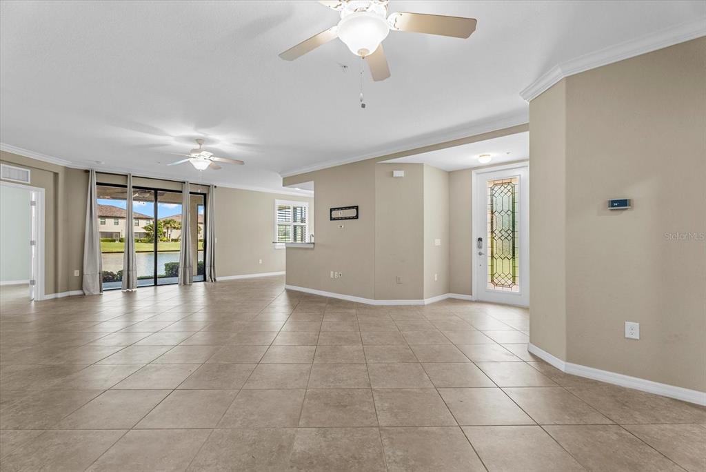 An open-concept living area features beige tile flooring, two ceiling fans, and a glass-paneled door — 20150 RAGAZZA CIRCLE UNIT 102, VENICE, FL