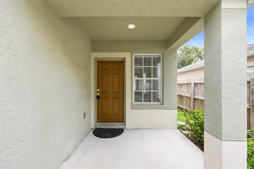 A covered concrete porch features a brown front door and a window with white blinds — 1717 MOSAIC FOREST DRIVE, SEFFNER, FL