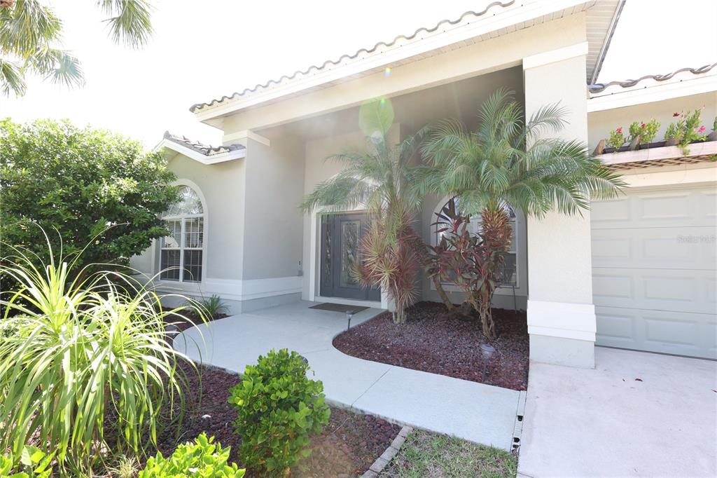 A beige house exterior features a covered entryway, a gray front door, and palm landscaping — 9826 WEATHER STONE PLACE, FORT MYERS, FL