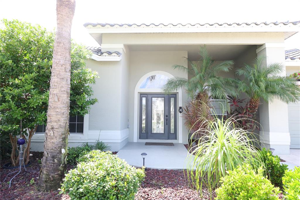 The exterior of a house features a gray front door, arched window, and palm trees — 9826 WEATHER STONE PLACE, FORT MYERS, FL