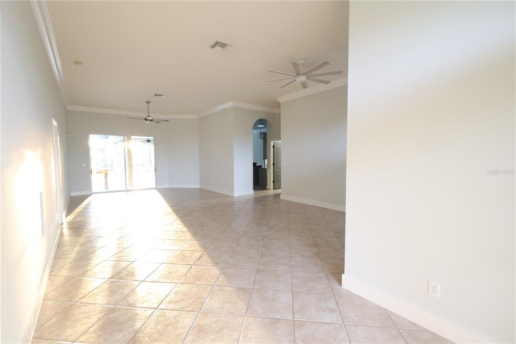 An open-concept living area features light-colored tile flooring, two ceiling fans, and sliding glass doors — 9826 WEATHER STONE PLACE, FORT MYERS, FL