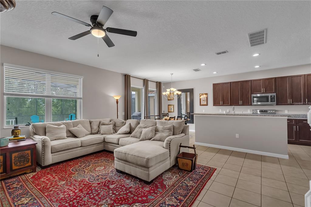 An open-concept living room features a beige sectional sofa, a red patterned rug, and a kitchen — 391 CABELLO DRIVE, DAVENPORT, FL