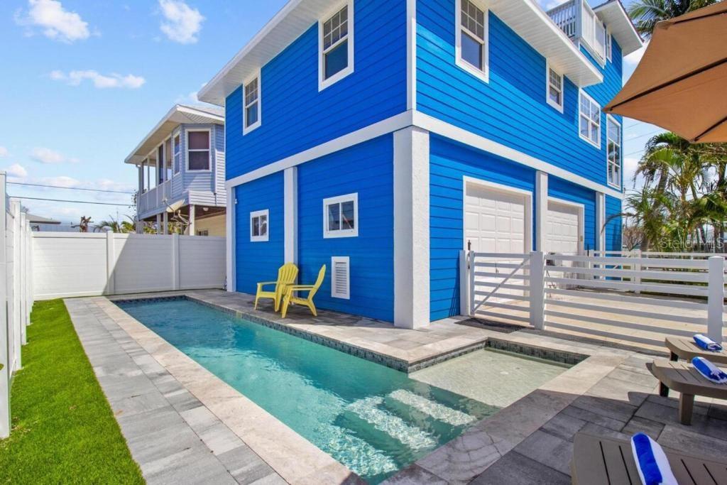 A bright blue multi-story house features a rectangular swimming pool with a shallow tanning ledge — 14500 N BAYSHORE DRIVE, MADEIRA BEACH, FL