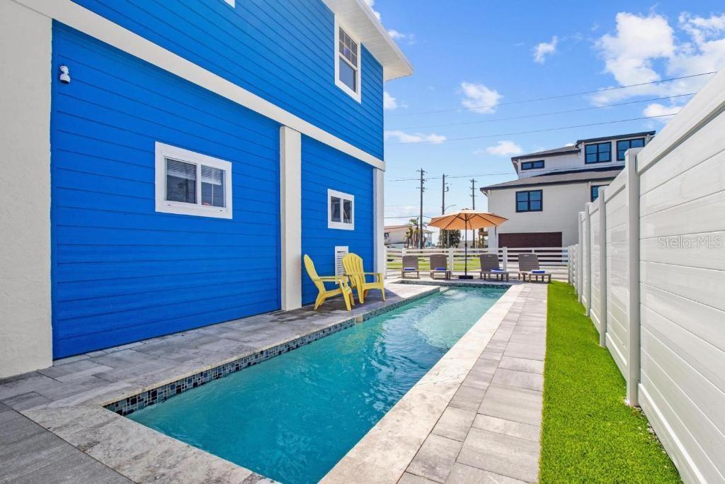 A narrow rectangular swimming pool sits beside a blue house with a white fence — 14500 N BAYSHORE DRIVE, MADEIRA BEACH, FL
