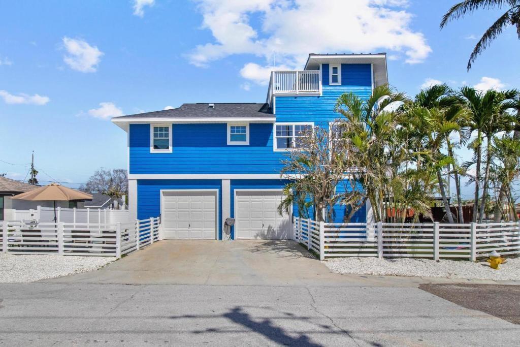 A bright blue, three-story house with two garage doors and a white picket fence — 14500 N BAYSHORE DRIVE, MADEIRA BEACH, FL