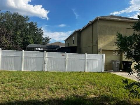 A white vinyl fence stands in front of a two-story tan house with a garage — 1034 LAKE DOE BOULEVARD, APOPKA, FL