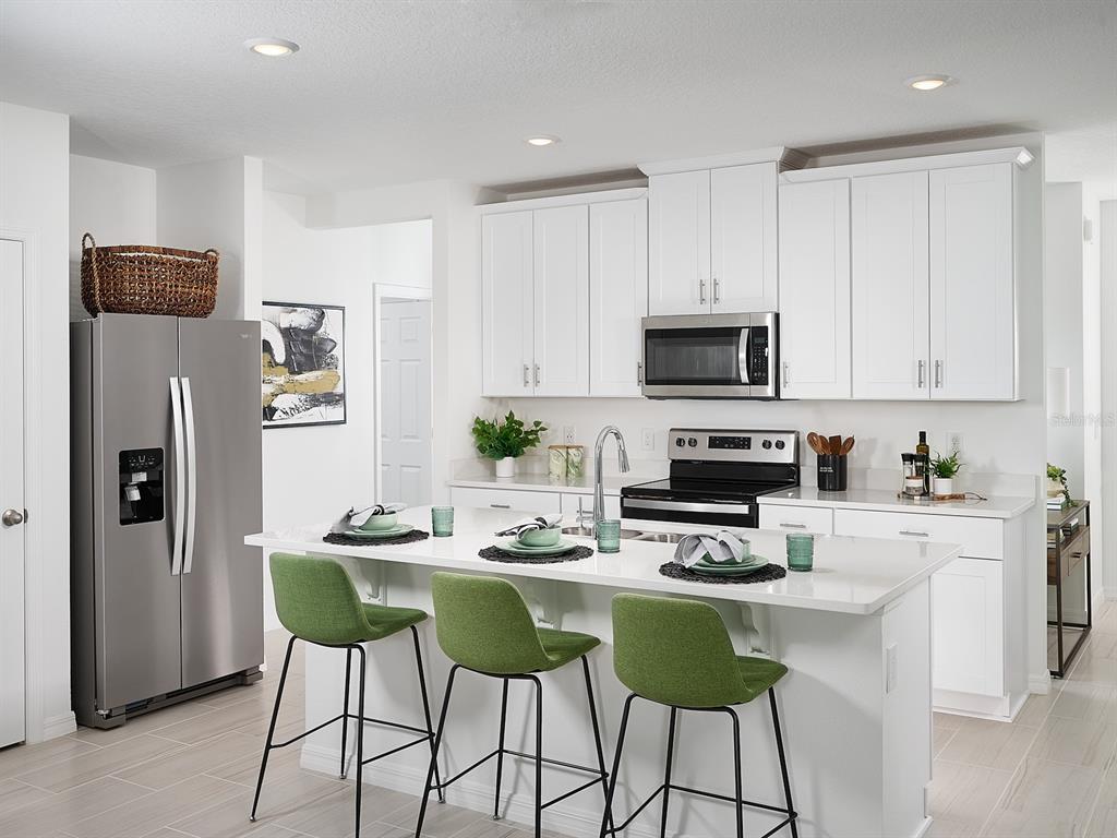 A modern kitchen features white cabinetry, stainless steel appliances, a quartz island, and green barstools — 3960 GIORGIO DRIVE, WINTER HAVEN, FL