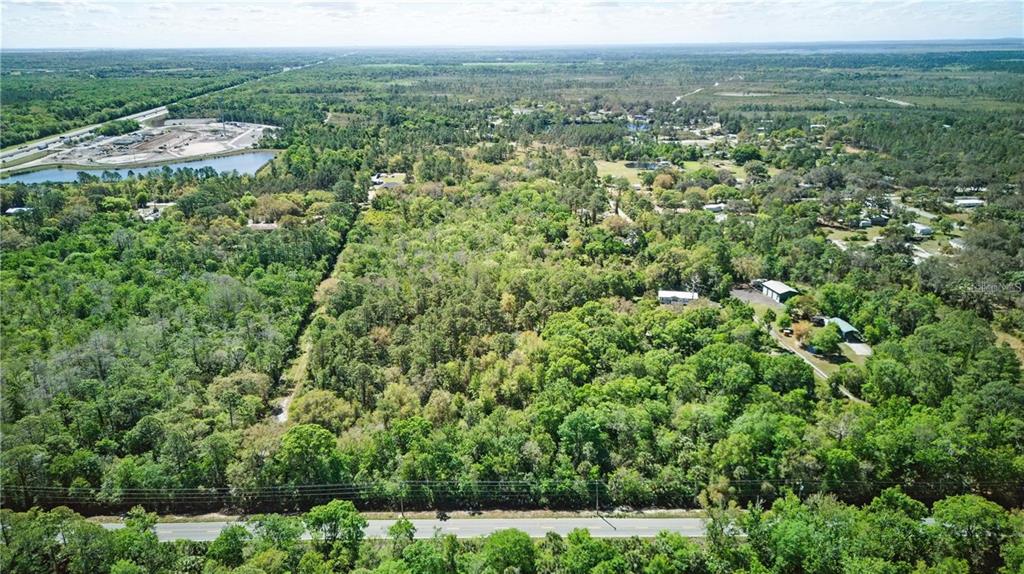 An aerial view shows a wooded lot bordered by a road with nearby residential development — HARRISON RD, MIMS, FL