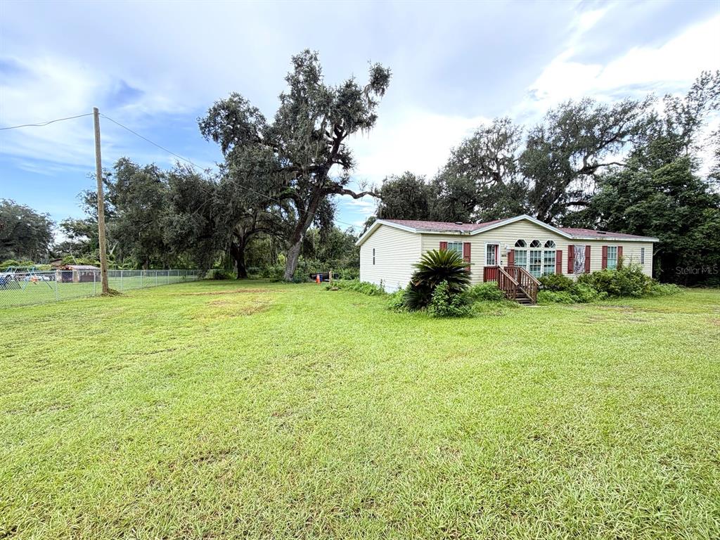 A single-story house with light siding stands on a large, grassy lot with mature trees — 36910 SUNSHINE ROAD, ZEPHYRHILLS, FL