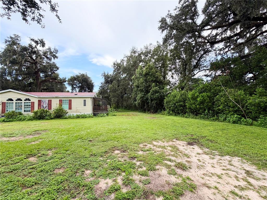 A light-colored mobile home sits on a grassy lot surrounded by large, mature trees — 36910 SUNSHINE ROAD, ZEPHYRHILLS, FL