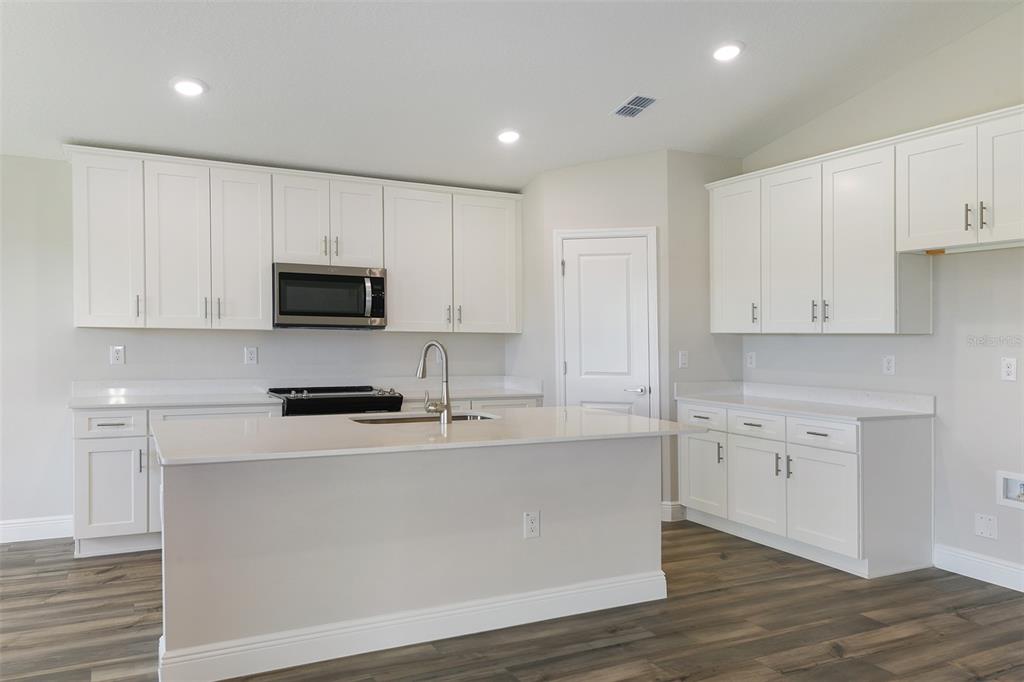 A modern kitchen features white cabinets, quartz countertops, a center island, and wood-look flooring — 6087 SW 97TH PLACE, OCALA, FL