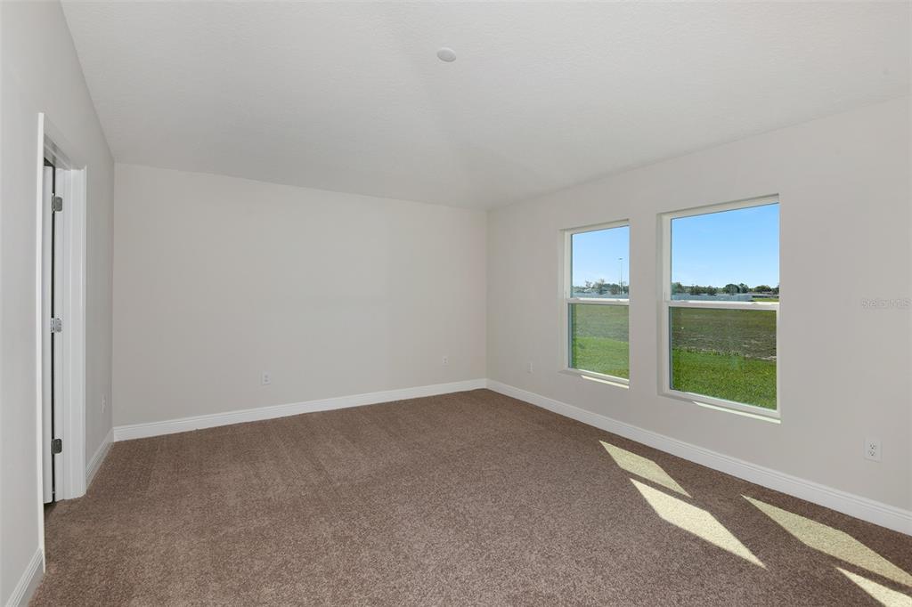 An empty bedroom with beige carpet, light-colored walls, and two windows overlooking a grassy field — 6087 SW 97TH PLACE, OCALA, FL