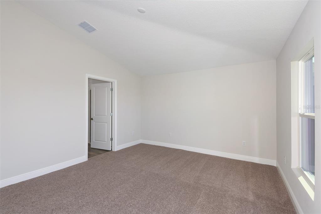 An empty bedroom with beige carpet, light-colored walls, a vaulted ceiling, and a doorway — 6087 SW 97TH PLACE, OCALA, FL