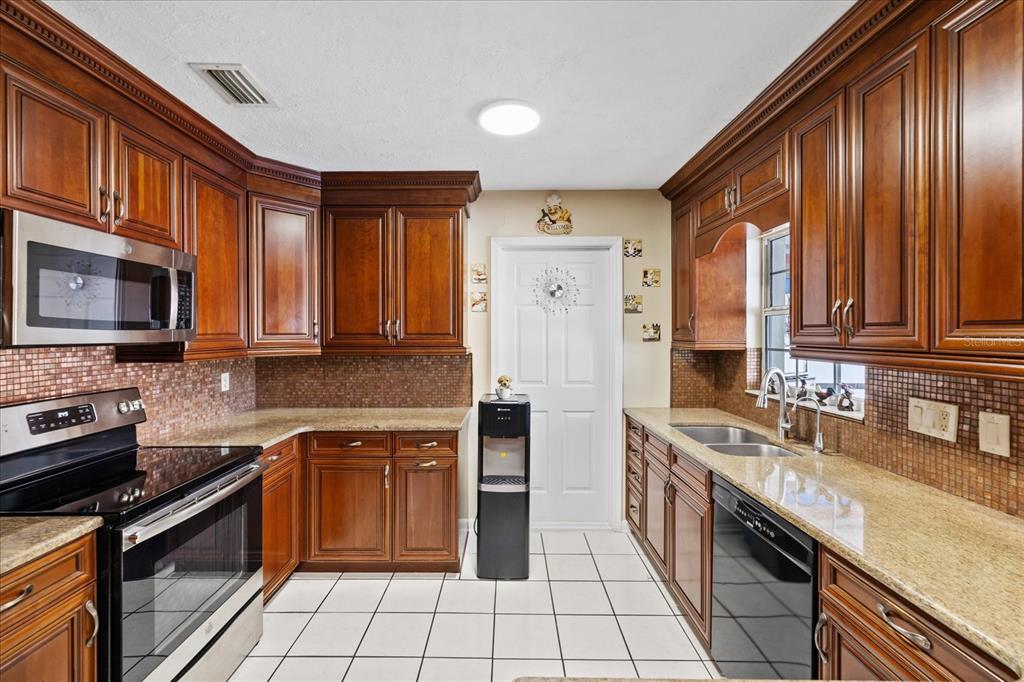 A kitchen with dark wood cabinets, granite countertops, stainless steel appliances, and white tile flooring — 5809 N HALE AVENUE, TAMPA, FL