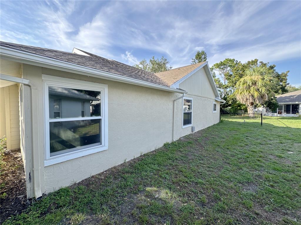 The exterior side of a beige stucco house features two windows and a grassy yard — 3174 57TH AVENUE CIRCLE E, BRADENTON, FL