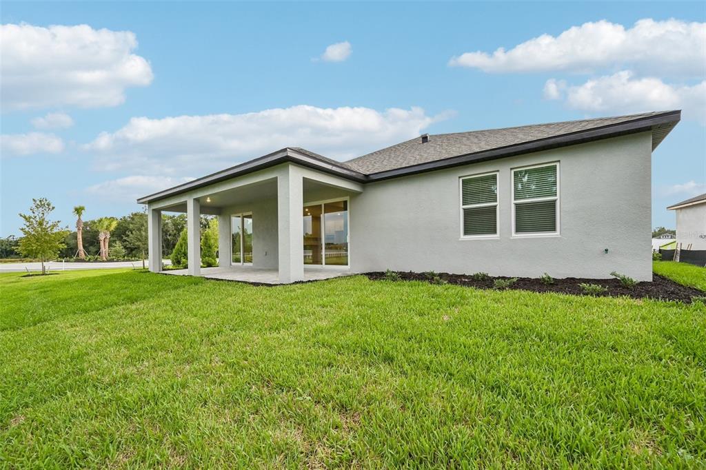 A rear exterior view of a single-story house with a covered patio and lawn — 3771 142ND TERRACE E, PARRISH, FL