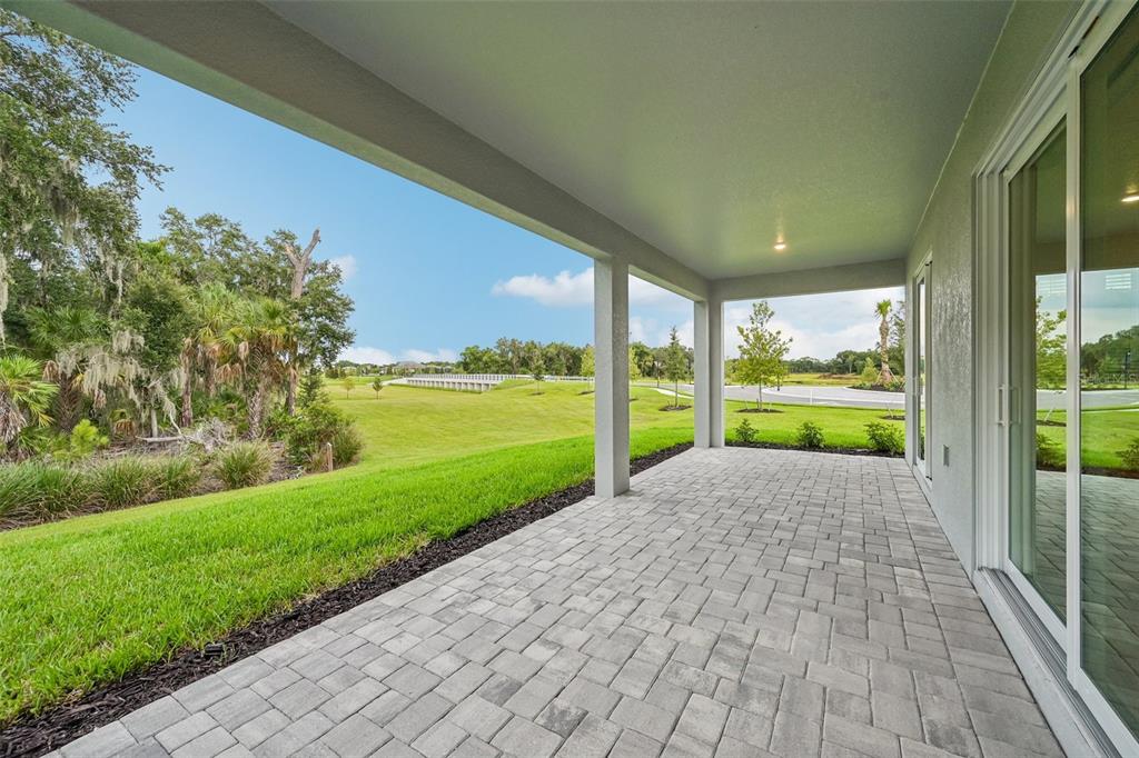 A covered patio with light gray pavers overlooks a grassy lawn and a wooded area — 3771 142ND TERRACE E, PARRISH, FL