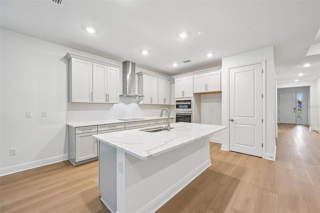 A modern kitchen features white cabinets, a marble-topped island, and light wood flooring — 3771 142ND TERRACE E, PARRISH, FL