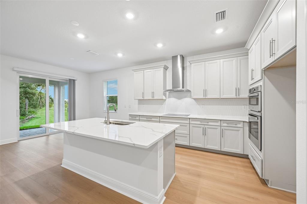 A modern kitchen with white cabinets, a marble-topped island, and a sliding glass door — 3771 142ND TERRACE E, PARRISH, FL