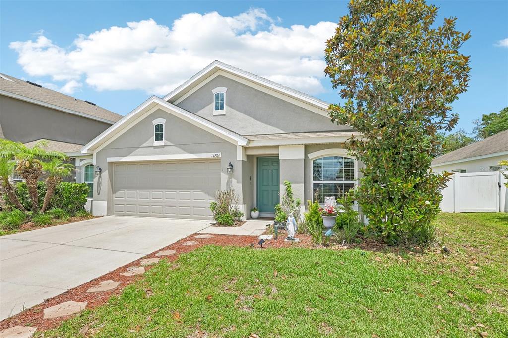 A single-story house with a gray stucco exterior, a two-car garage, and a teal front door — 14284 FINSBURY DRIVE, SPRING HILL, FL