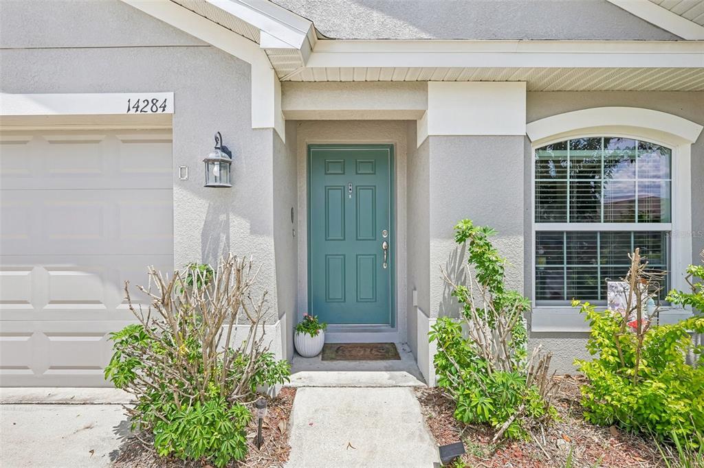 The exterior of a house features a teal front door, a garage, and landscaping — 14284 FINSBURY DRIVE, SPRING HILL, FL