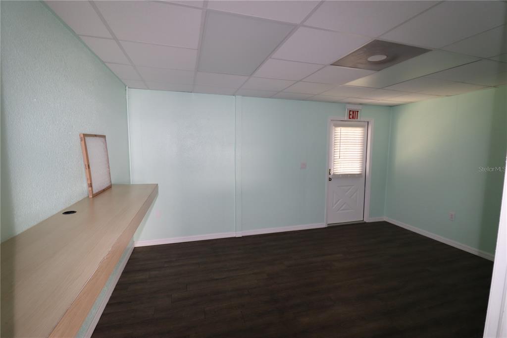 An empty room features light green walls, dark wood-look flooring, a drop ceiling, and a desk — 18350 PAULSON DRIVE UNIT D-2, PORT CHARLOTTE, FL