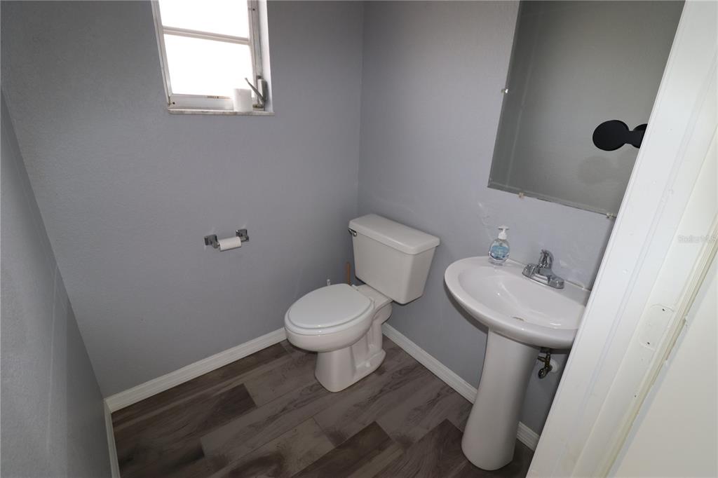 A small bathroom features gray walls, wood-look flooring, a white pedestal sink, and a toilet — 18350 PAULSON DRIVE UNIT D-2, PORT CHARLOTTE, FL