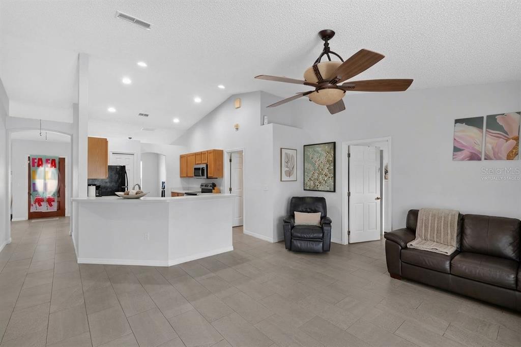 A living room with tile flooring, a ceiling fan, and an open kitchen with wood cabinets — 1906 MANATEE LANE, KISSIMMEE, FL