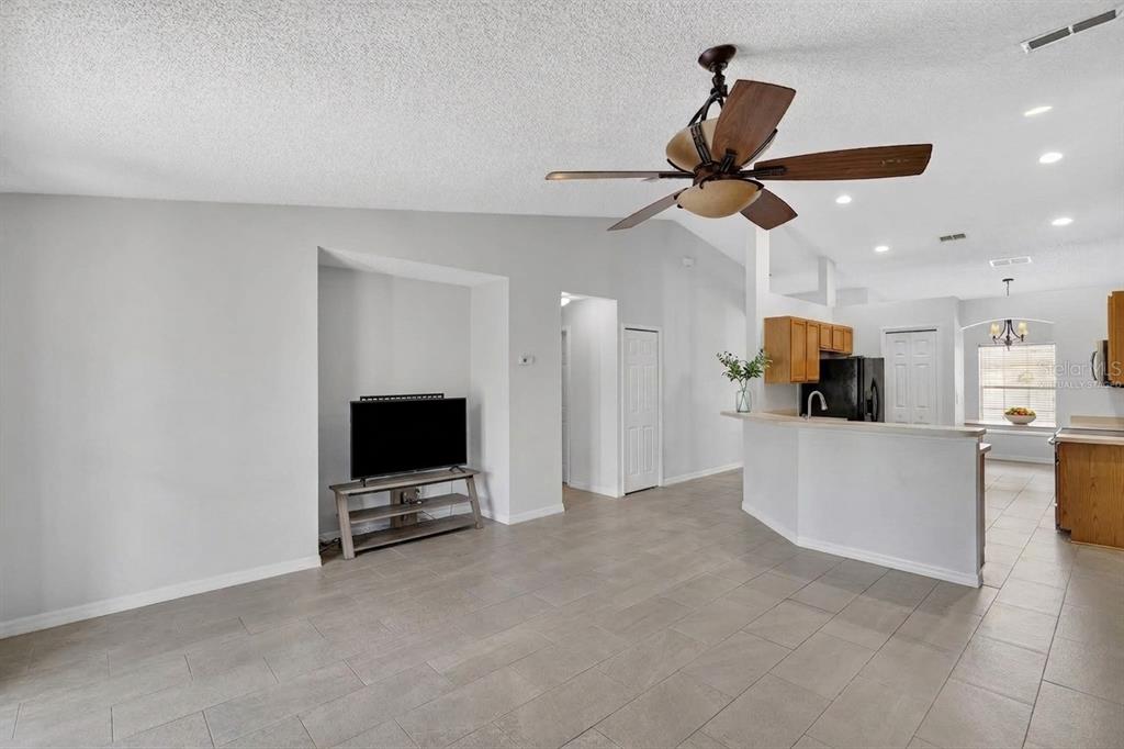 A living room with tile flooring, a ceiling fan, and an open kitchen with wooden cabinets — 1906 MANATEE LANE, KISSIMMEE, FL