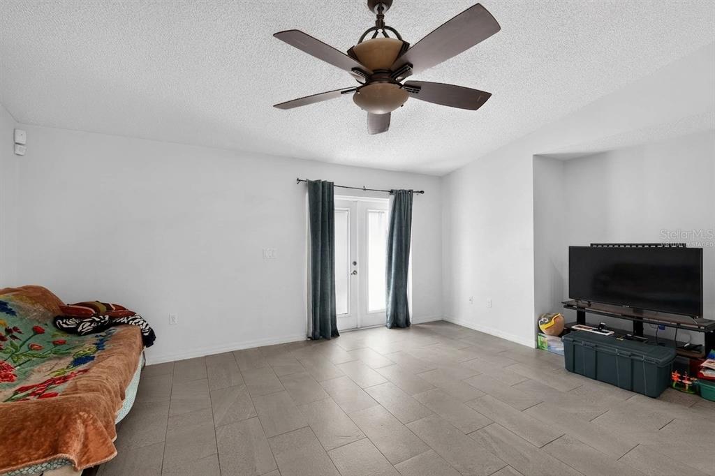 A living room features light tile floors, white walls, a ceiling fan, and glass doors — 1906 MANATEE LANE, KISSIMMEE, FL