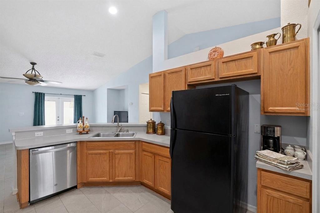 A kitchen features oak cabinets, stainless steel appliances, a black refrigerator, and light gray countertops — 1906 MANATEE LANE, KISSIMMEE, FL