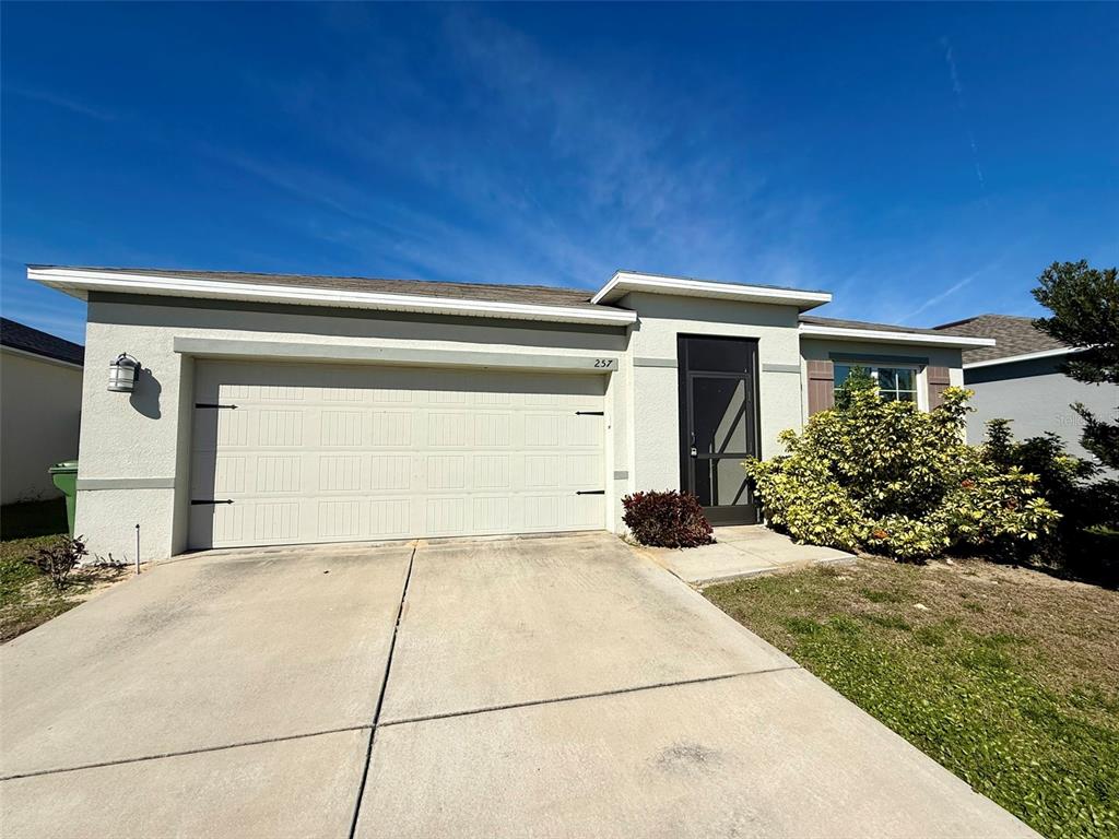A single-story house features a two-car garage, a front entryway with a screen door, and landscaping — 257 MEADOWBROOK BOULEVARD, WINTER HAVEN, FL