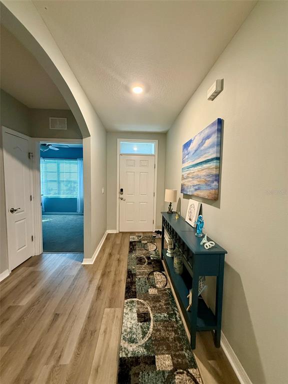 A hallway with wood-look flooring leads to a white front door and a side room — 257 MEADOWBROOK BOULEVARD, WINTER HAVEN, FL